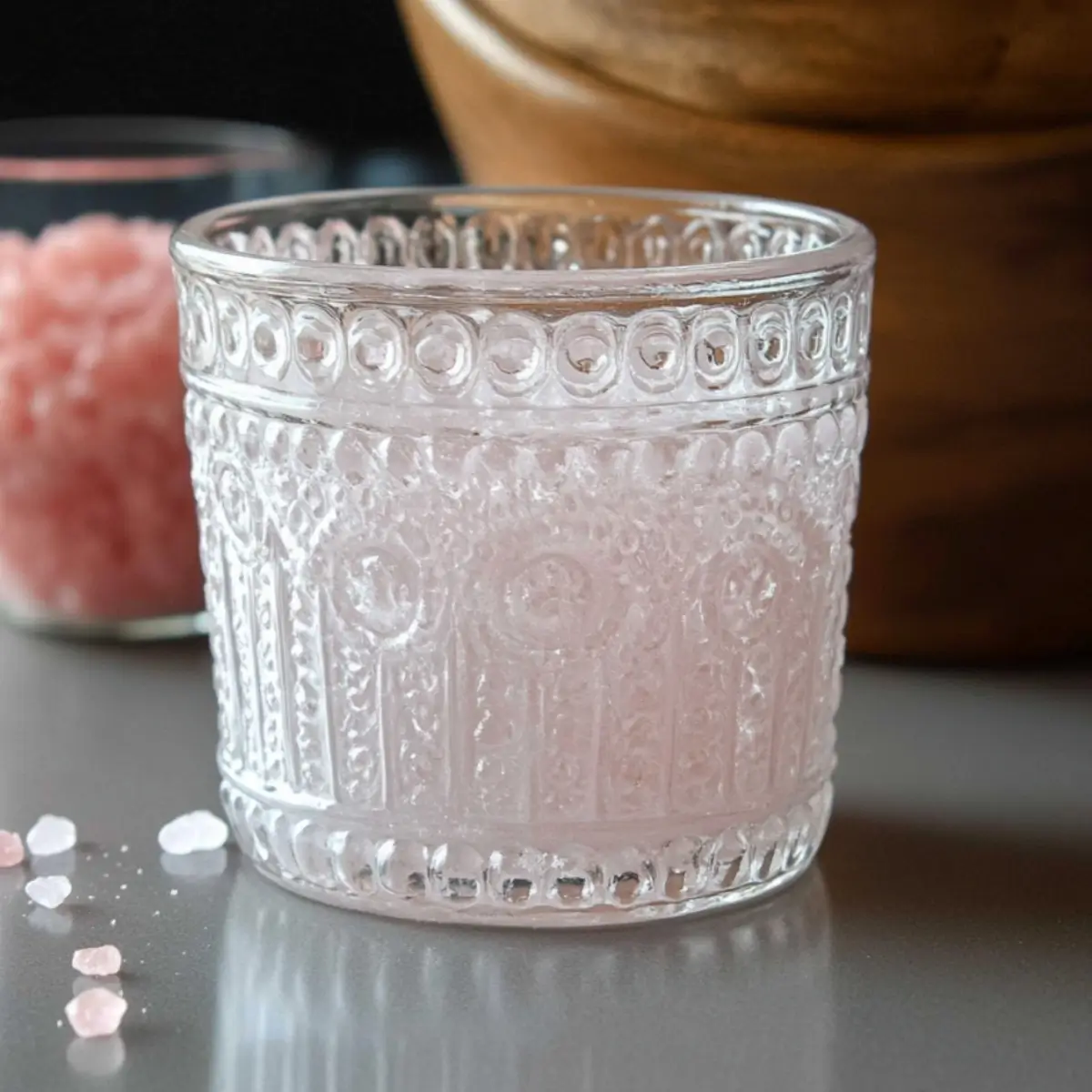 Woman preparing pink salt trick recipe in kitchen with pink Himalayan salt dissolving in clear glass of water