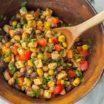 Southwest dense bean salad with black beans, pinto beans, corn, bell peppers, and cilantro lime dressing in wooden bowl